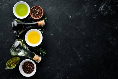 Zeytin yağı, ayçiçeği yağı ve biberiye. Siyah taş arka planda. Üst görünüm. Ücretsiz kopya alanı.