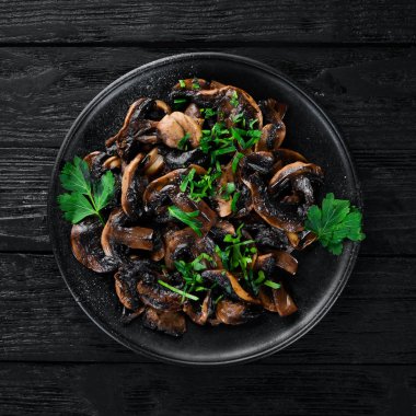 Tabak üzerinde maydanoz ile kızarmış mantar. Siyah bir arka planda. Üst görünüm. Metniniz için boş alan.