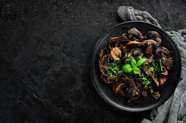 Tabak üzerinde maydanoz ile kızarmış mantar. Siyah bir arka planda. Üst görünüm. Metniniz için boş alan.