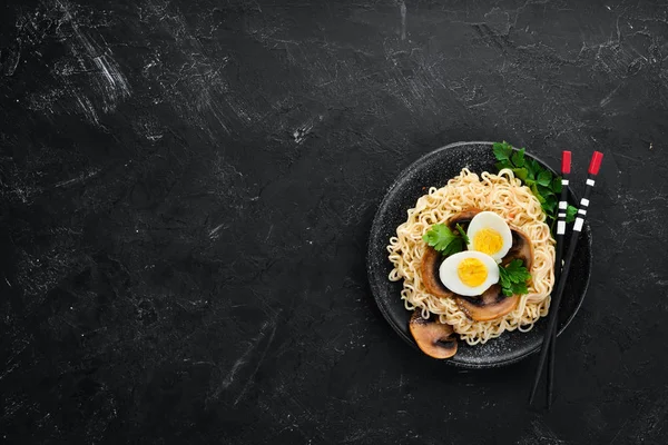 Asian food. Noodles with mushrooms, eggs and chia seeds. On a black stone background. Top view. Free copy space.