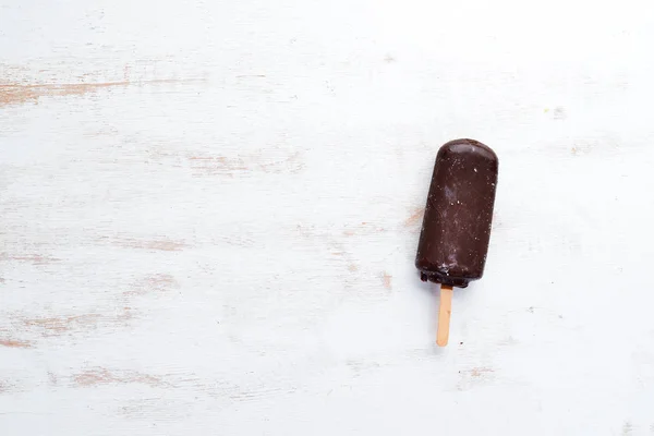 Chocolate ice cream on a stick. On a white wooden background. Top view. Free copy space.