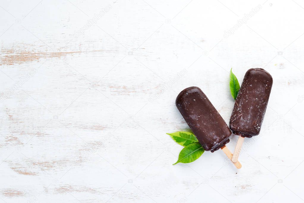 Chocolate ice cream on a stick. On a white wooden background. Top view. Free copy space.