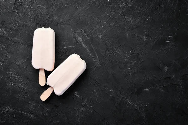 Ice-cream on a stick with white chocolate. On a black background. Top view. Free copy space.