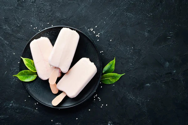 Ice-cream on a stick with white chocolate. On a black background. Top view. Free copy space.