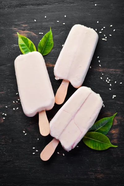 Ice-cream on a stick with white chocolate. On a black background. Top view. Free copy space.