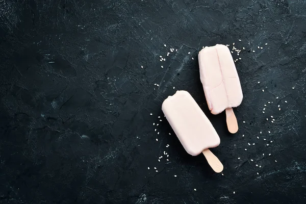 Ice-cream on a stick with white chocolate. On a black background. Top view. Free copy space.