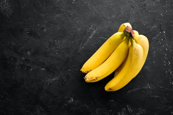 stock image Fresh yellow bananas on a black stone table. Top view. Free copy space.