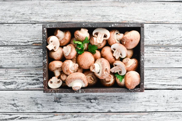 Mushrooms in a wooden box on the old table. Champignons Top view. Free copy space.