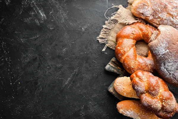 Assortment of bread and baking on a black stone background. Top view. Free space for your text.