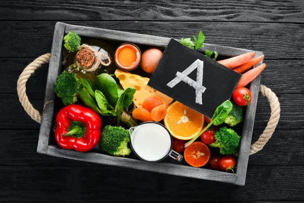 Foods containing natural Vitamin A: broccoli, carrots, milk, cheese, spinach, apricots, parsley, tomatoes. On a black stone kitchen background. Top view.