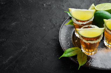 Siyah taş arka plan üzerinde kireç ve tuz ile altın tekila. Üst te. Metniniz için boş alan.