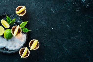 Siyah taş arka plan üzerinde kireç ve tuz ile altın tekila. Üst te. Metniniz için boş alan.