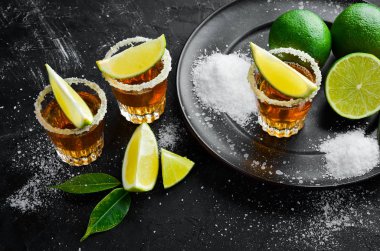 Siyah taş arka plan üzerinde kireç ve tuz ile altın tekila. Üst te. Metniniz için boş alan.