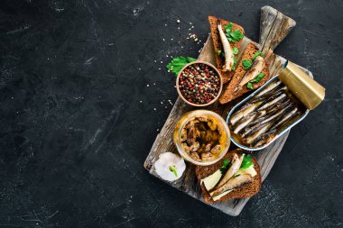 Yağda sprats çeşitleri. Füme balık Siyah bir arka plan üzerinde. üst görünüm. Ücretsiz kopyalama alanı.
