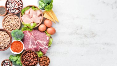 Masada protein oranı yüksek olan yiyecekler. Et, tavuk filetosu, brokoli, fasulye, peynir, yumurta, buğday. Beyaz ahşap arka planda.