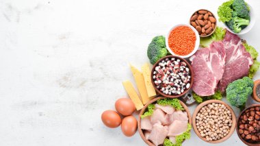 Masada protein oranı yüksek olan yiyecekler. Et, tavuk filetosu, brokoli, fasulye, peynir, yumurta, buğday. Beyaz ahşap arka planda.