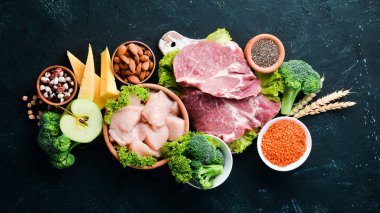 Sağlıklı protein kaynağı ve vücut geliştirme gıdaların çeşitleri. Et, tavuk filetosu, brokoli, fasulye, peynir, yumurta, buğday. Taş arka planda.