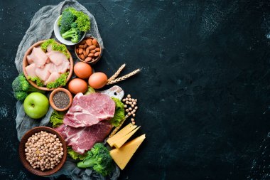 Sağlıklı protein kaynağı ve vücut geliştirme gıdaların çeşitleri. Et, tavuk filetosu, brokoli, fasulye, peynir, yumurta, buğday. Taş arka planda.