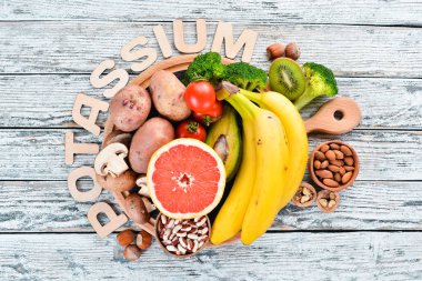 Doğal potasyum içeren gıdalar. K: Patates, mantar, muz, domates, fındık, fasulye, brokoli, avokado. Üst te. Beyaz ahşap arka planda.
