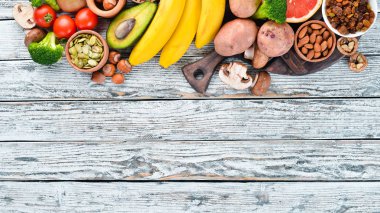 Doğal potasyum içeren gıdalar. K: Patates, mantar, muz, domates, fındık, fasulye, brokoli, avokado. Üst te. Beyaz ahşap arka planda.