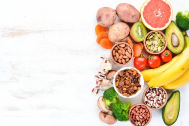 Doğal potasyum içeren gıdalar. K: Patates, mantar, muz, domates, fındık, fasulye, brokoli, avokado. Üst te. Beyaz ahşap arka planda.