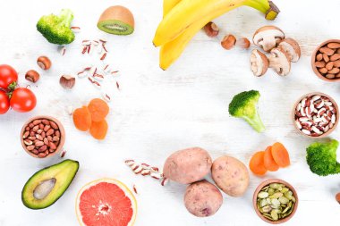 Doğal potasyum içeren gıdalar. K: Patates, mantar, muz, domates, fındık, fasulye, brokoli, avokado. Üst te. Beyaz ahşap arka planda.