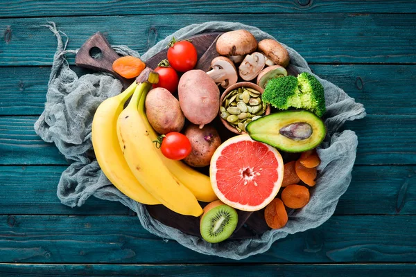 Foods containing natural potassium. K: Potatoes, mushrooms, banana, tomatoes, nuts, beans, broccoli, avocados. Top view. On a blue wooden background.