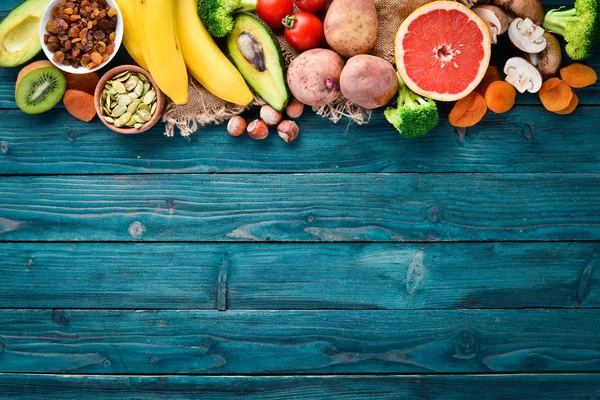 Foods containing natural potassium. K: Potatoes, mushrooms, banana, tomatoes, nuts, beans, broccoli, avocados. Top view. On a blue wooden background.