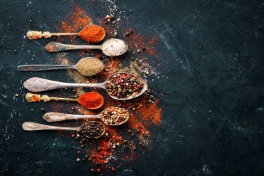 Kaşıkta biber. Renkli biber, deniz tuzu, karabiber, acı biber. Üst te. Siyah arka planda.