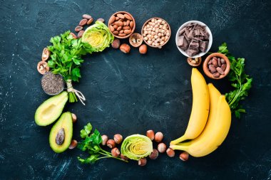 Doğal magnezyum içeren gıdalar. Mg: Çikolata, muz, kakao, fındık, avokado, brokoli, badem. Üst te. Siyah arka planda.