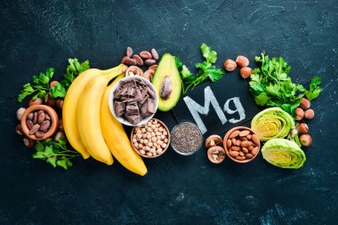 Doğal magnezyum içeren gıdalar. Mg: Çikolata, muz, kakao, fındık, avokado, brokoli, badem. Üst te. Siyah arka planda.