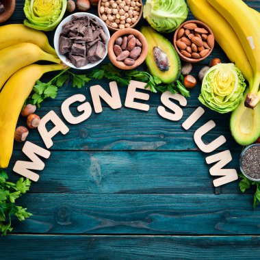 Doğal magnezyum içeren gıdalar. Mg: Çikolata, muz, kakao, fındık, avokado, brokoli, badem. Üst te. Mavi ahşap arka planda.