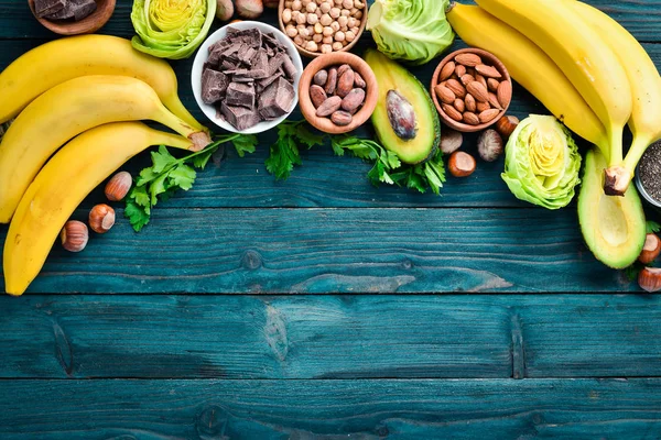 天然マグネシウムを含む食品 チョコレート バナナ ココア ナッツ アボカド ブロッコリー アーモンド トップビュー 青い木製の背景に — ストック写真