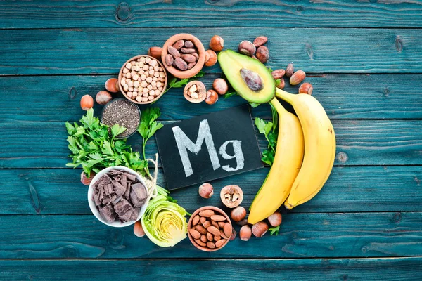 Doğal magnezyum içeren gıdalar. Mg: Çikolata, muz, kakao, fındık, avokado, brokoli, badem. Üst te. Mavi ahşap arka planda.