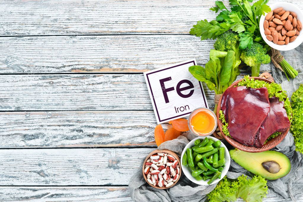 Food containing natural iron. Fe: Liver, avocado, broccoli, spinach, parsley, beans, nuts, on a white wooden background. Top view.