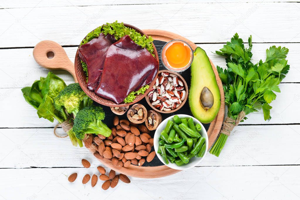 Food containing natural iron. Fe: Liver, avocado, broccoli, spinach, parsley, beans, nuts, on a white wooden background. Top view.
