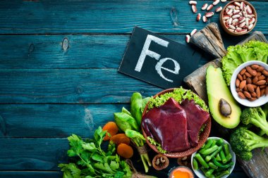 Doğal demir içeren yiyecekler. Fe: Karaciğer, avokado, brokoli, ıspanak, maydanoz, fasulye, fındık, mavi bir arka plan üzerinde. Üstte görüntü.