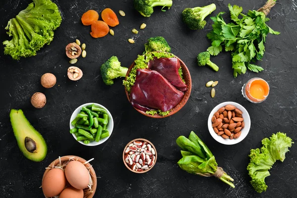 Food containing natural iron. Fe: Liver, avocado, broccoli, spinach, parsley, beans, nuts, on a black stone background. Top view.