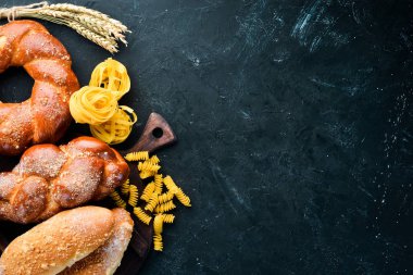 Glütensiz yiyecekler. Siyah taş arka planda ekmek, makarna ve un. Üst te. Metniniz için boş alan.