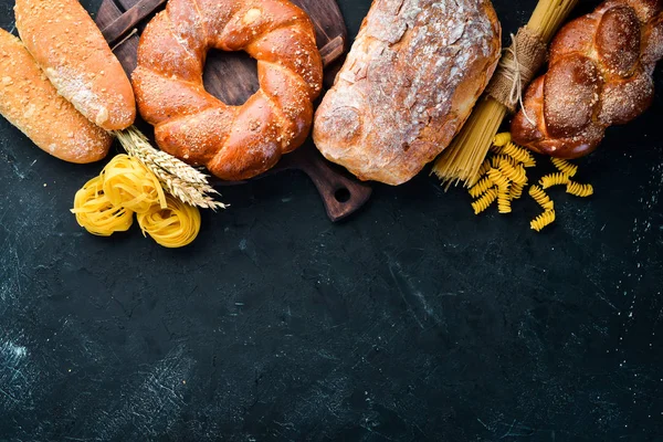 Glütensiz yiyecekler. Siyah taş arka planda ekmek, makarna ve un. Üst te. Metniniz için boş alan.