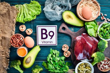 Doğal B9 vitamini içeren gıdalar: Karaciğer, avokado, brokoli, ıspanak, maydanoz, fasulye, fındık, mavi bir arka plan üzerinde. Üstte görüntü.