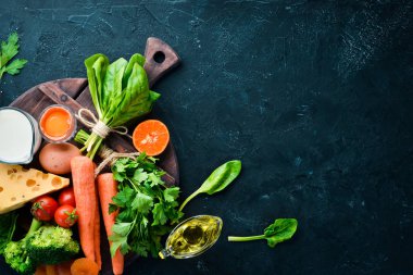 Sağlıklı gıdalar, meyve ve sebzeler. Brokoli, havuç, süt, peynir, ıspanak, kuru kayısı, maydanoz, domates. Üstte görüntü.