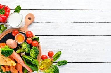 Sağlıklı gıdalar, meyve ve sebzeler. Brokoli, havuç, süt, peynir, ıspanak, kuru kayısı, maydanoz, domates. Üstte görüntü.