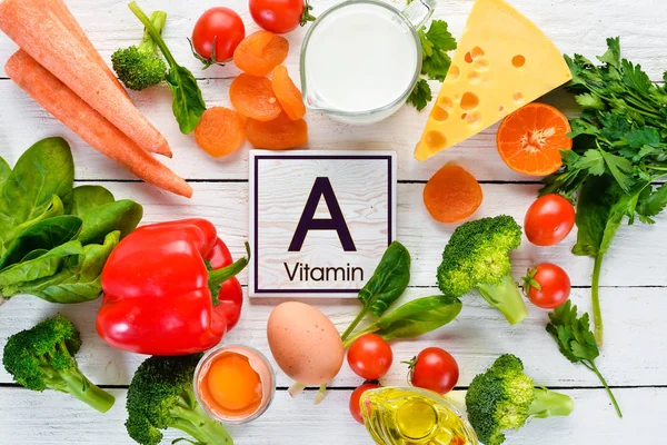 Foods containing natural Vitamin A: broccoli, carrots, milk, cheese, spinach, apricots, parsley, tomatoes. On a white wooden background. Top view.