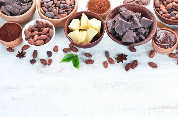 Cocoa beans, chocolate, cocoa butter and cocoa powder on a white wooden background. Top view. Free copy space.