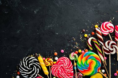 Renkli şekerler ve lolipoplar. Siyah taş bir arka plan üzerinde. Üst te. ücretsiz kopyalama alanı.