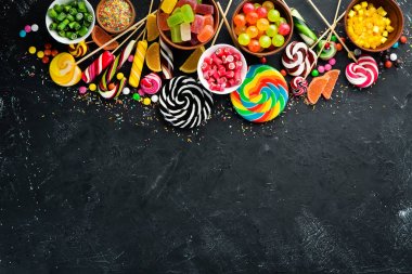 Renkli şekerler ve lolipoplar. Siyah taş bir arka plan üzerinde. Üst te. ücretsiz kopyalama alanı.