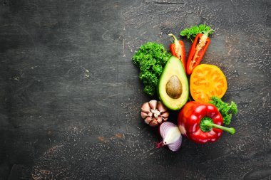 Siyah bir arka plan üzerinde taze sebze. Avokado, domates, sarımsak, maydanoz, kırmızı biber. Üst te. Metniniz için boş alan.