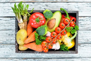 Tahta bir kutuda sebzeler. Avokado, salatalık, soğan, sarımsak, domates, havuç, yabanturpu. Üst te. Metniniz için boş alan.