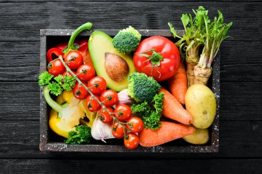 Tahta bir kutuda sebzeler. Avokado, salatalık, soğan, sarımsak, domates, havuç, yabanturpu. Üst te. Metniniz için boş alan.